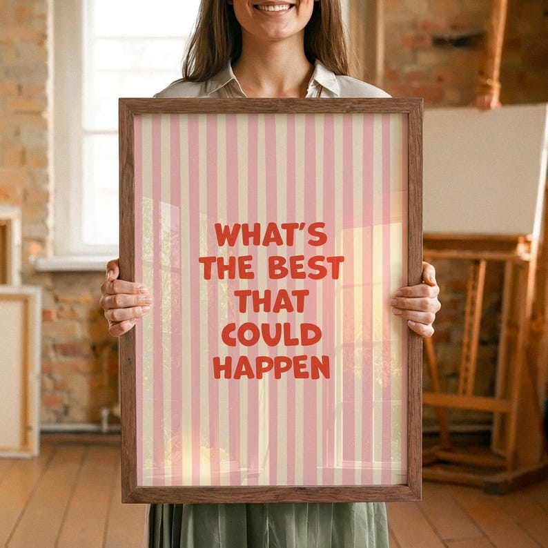 May include: A framed print with a pink and cream striped background. The text "WHAT'S THE BEST THAT COULD HAPPEN" is in red. The frame is brown.
