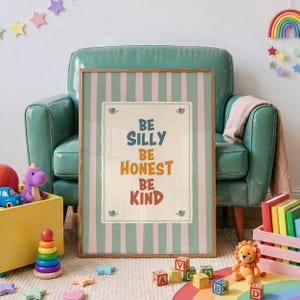 May include: A framed vertical wall art print featuring a light pink and teal vertical striped background. The centre contains a white rectangular panel with the text BE SILLY, BE HONEST, BE KIND in blue, orange, and red lettering with small bird icons.