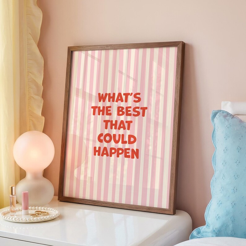 May include: A framed print with a pink and white striped background and the text "WHAT'S THE BEST THAT COULD HAPPEN" in red. The frame is a dark brown color. The print is displayed on a white nightstand.