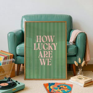 May include: A framed art print with the text "HOW LUCKY ARE WE" in pink letters on a green striped background. The print is displayed in a room with a teal armchair, a record player, and vinyl records.