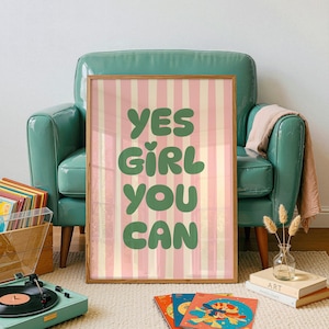 May include: A framed art print with the text "YES GIRL YOU CAN" in green letters on a pink and white striped background. The print is displayed in a room with a teal armchair, a record player, and books.