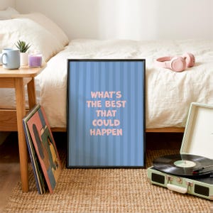 Puede incluir: Un p&oacute;ster enmarcado con el texto "WHAT'S THE BEST THAT COULD HAPPEN" en letras rosas sobre un fondo azul a rayas. El p&oacute;ster est&aacute; en un marco negro y est&aacute; apoyado contra una cama. Tambi&eacute;n se ven un tocadiscos y unos auriculares.