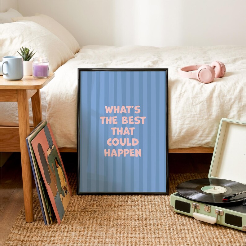 Puede incluir: Un p&oacute;ster enmarcado con el texto "WHAT'S THE BEST THAT COULD HAPPEN" en letras rosas sobre un fondo azul a rayas. El p&oacute;ster est&aacute; en un marco negro y est&aacute; apoyado contra una cama. Tambi&eacute;n se ven un tocadiscos y unos auriculares.