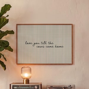May include: A rectangular wall art piece in a wooden frame featuring a light green and white vertical striped background with the black cursive text "love you till the cows come home" centered horizontally across the middle of the print.