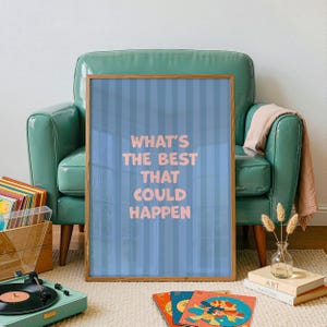 Puede incluir: Un p&oacute;ster enmarcado con el texto "WHAT'S THE BEST THAT COULD HAPPEN" en letras rosas sobre un fondo azul a rayas. El p&oacute;ster est&aacute; apoyado contra un sill&oacute;n verde azulado. Un tocadiscos y discos de vinilo est&aacute;n en primer plano.