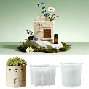 May include: A ceramic planter in the shape of a miniature building, inscribed with "CAFE". It's filled with flowers and rests on a rock base. An essential oil bottle is placed nearby. Additional planters are also shown.