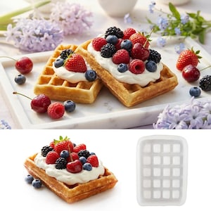 Puede incluir: Gofres dorados cubiertos con crema batida, fresas, frambuesas, arándanos y moras. Los gofres están colocados en una bandeja de mármol blanco, con bayas frescas y flores en el fondo. También se muestra un molde de silicona para gofres.
