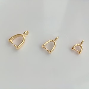 Op de afbeelding: Drie gouden metalen hangerbedels in verschillende maten. De bedels zijn gevormd als een kleine boog met een lus aan de bovenkant.