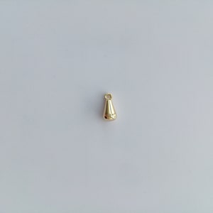May include: A gold-colored metal pendant shaped like a teardrop with a small loop at the top.