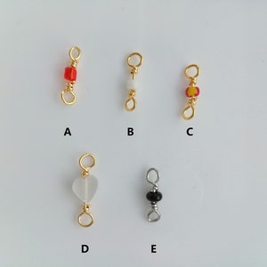 Puede incluir: Cinco tipos diferentes de conectores de cuentas y anillos de salto de oro y plata. Los conectores están etiquetados de la A a la E. El conector A tiene una cuenta roja, B tiene una cuenta blanca, C tiene una cuenta roja y amarilla, D tiene una cuenta blanca en forma de corazón y E tiene una cuenta negra.