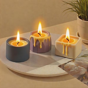 May include: Three lit candles with a melted wax design. The candles are in different geometric shapes: a cylinder, a hexagon, and a square. The candle colors are gray, purple, and cream. The wax is yellow and dripping down the sides. A small plant is in the background.