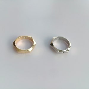 May include: Two hexagonal rings, one gold and one silver, on a white background.