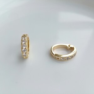 May include: A pair of gold hoop earrings with clear cubic zirconia stones.