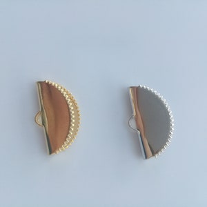 May include: Two half-circle metal clasps, one gold and one silver, with a scalloped edge.