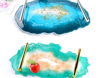 May include: Two resin serving trays with gold leaf accents and metal handles. The top tray is oval shaped and blue with white accents. The bottom tray is a more irregular shape and is green with white and pink accents.