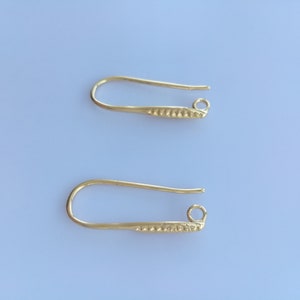 Puede incluir: Dos ganchos para pendientes de color dorado con un diseño texturizado. Los ganchos son de metal y tienen un pequeño bucle en el extremo.