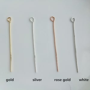 May include: Four head pins in different metal finishes: gold, silver, rose gold, and white gold. The pins are straight and have a small loop at the top.