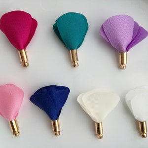 May include: Assortment of eight fabric flower embellishments with gold metal stems. The flowers are in pink, white, purple, teal, blue, and red.