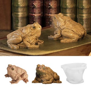 May include: Two detailed frog figurines in shades of brown and tan are displayed on a surface. The frogs are sculpted with textured skin and realistic features. The image also shows a smaller frog figurine and a white container.