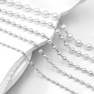 May include: A collection of five silver-toned metal chains featuring evenly spaced white faux pearl beads. The chains vary in bead size and are arranged in parallel lines, showcasing a delicate link design connecting each individual round pearl bead.