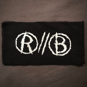 May include: Black fabric patch with white embroidered circles containing the letters "R" and "B" with slashes between them.