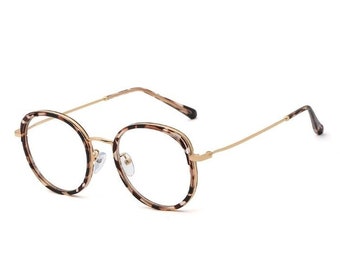 Puede incluir: Gafas redondas con un patrón de carey en las monturas y patillas. Las monturas son de color marrón claro con varillas y puente nasal de metal dorado. Las lentes son transparentes.