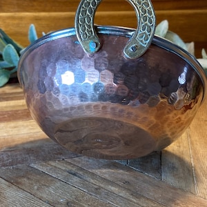 May include: A hammered copper bowl with a decorative brass handle. The bowl has a rustic, antique look and is perfect for serving snacks or dips.