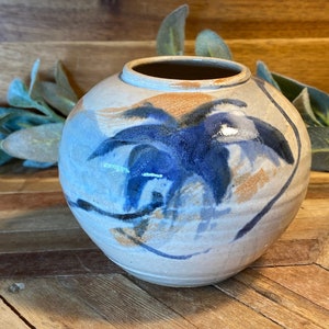 May include: A small, round ceramic vase with a blue and brown abstract design. The vase has a white glaze and a slightly textured surface.