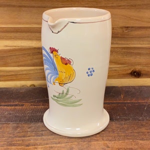 May include: White ceramic pitcher with a rooster design. The rooster is yellow with blue and red accents. The pitcher has a green leaf design and blue flowers.