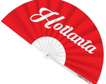 May include: A red hand fan with the word "Atlanta" in white script. The fan is open, displaying a radial pattern. The handle and the fan's internal structure are white. The text "THEGAYFANCLUB.COM" is printed on the handle.