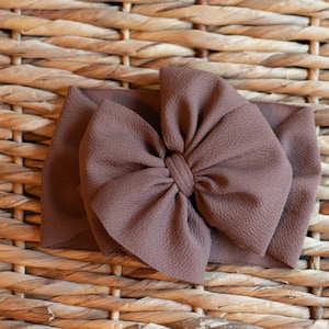 May include: A brown fabric headband with a large, knotted bow. The headband is on a woven wicker background.
