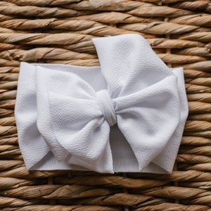 May include: A white fabric headband with a large, fluffy bow. The headband is made of a soft, stretchy material and is perfect for adding a touch of style to any outfit.