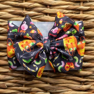 Peut inclure: Un nœud pour cheveux noir et orange sur le thème d'Halloween avec une variété de motifs effrayants et amusants, notamment du maïs sucré, des citrouilles et des vers.