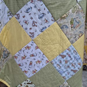 May include: A patchwork quilt featuring a variety of fabric squares. Some squares are solid yellow, others are olive green with white polka dots, and several feature printed illustrations of Winnie the Pooh characters including Eeyore and Tigger.