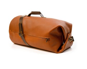May include: A brown leather duffel bag with a top handle and a shoulder strap. The bag has a zippered side pocket and metal hardware. The leather has a textured appearance.