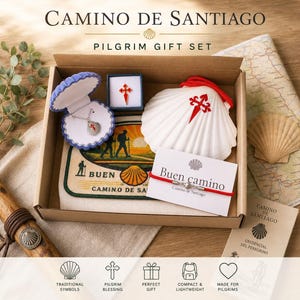 Könnte beinhalten: Ein Camino de Santiago Pilger-Geschenkset in einem Karton, bestehend aus einer muschelförmigen Schmuckschatulle mit Halskette, einer kleinen roten Kreuz-Anstecknadel, einer großen weißen Jakobsmuschel mit rotem Kreuz und einem roten Armband.