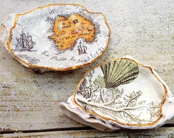 May include: Two decorative oyster shells with gold trim. One shell features a vintage map with a ship and the text "Le Passe de tous les D", the other shell features a vintage illustration of a seashell and seaweed.