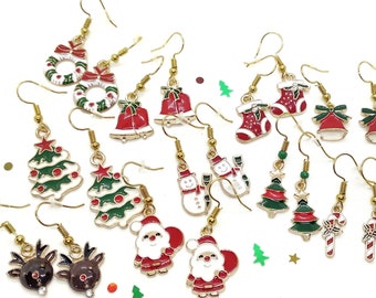 May include: A collection of gold-toned metal hook earrings featuring colorful enamel Christmas-themed charms including Santa Claus, snowmen, reindeer, Christmas trees, wreaths, stockings, bells, and candy canes, arranged on a plain white surface.