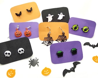 Op de afbeelding: Assortiment van Halloween-oorbellen op displaykaarten. De oorbellen hebben verschillende ontwerpen, waaronder pompoenen, schedels, vleermuizen, geesten, spinnen en ketels. De kaarten zijn in verschillende kleuren, waaronder oranje, paars en zwart.