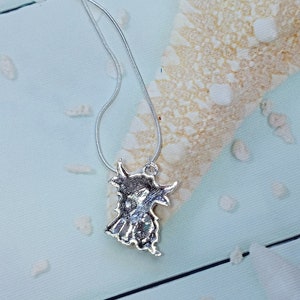 May include: A silver-toned metal pendant shaped like a Highland cow, featuring textured detailing on the surface, suspended from a thin silver-toned snake chain necklace. The pendant displays the distinct silhouette of the animal with horns.