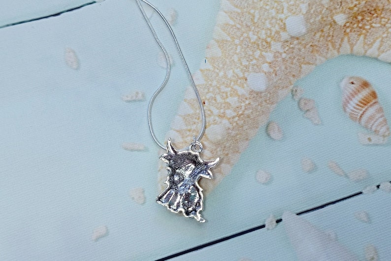 May include: A silver-toned metal pendant shaped like a Highland cow, featuring textured detailing on the surface, suspended from a thin silver-toned snake chain necklace. The pendant displays the distinct silhouette of the animal with horns.