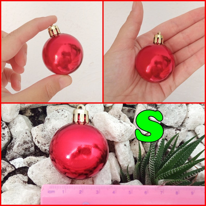 May include: A shiny red Christmas ornament with a gold cap. The ornament is shown in different views, including held in a hand and resting on white stones. A green letter "S" is also visible.