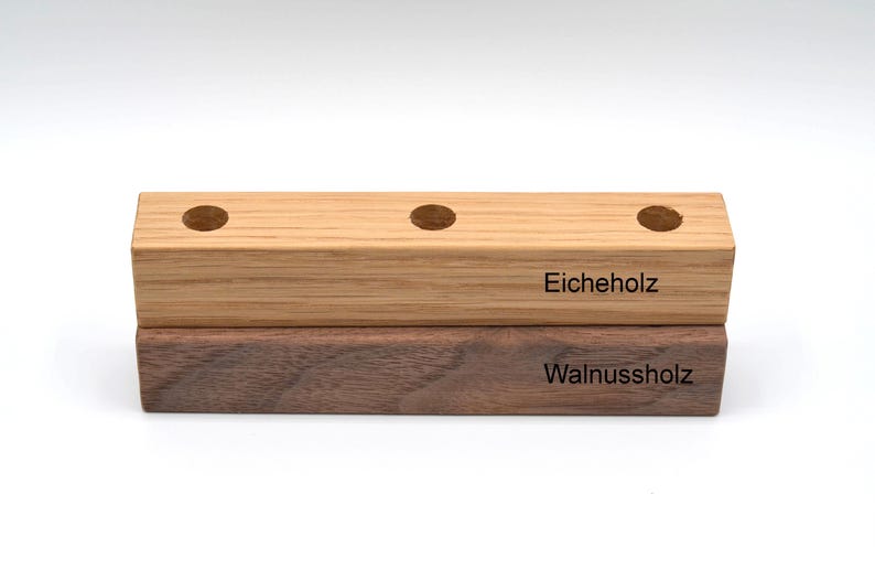 May include: Two wooden blocks stacked on top of each other. The top block is light brown and says "Eicheholz". The bottom block is dark brown and says "Walnuss holz".