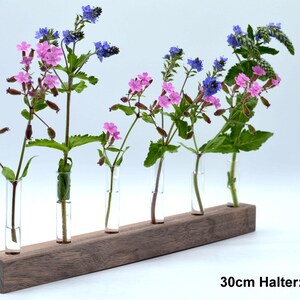 May include: A wooden flower holder with five glass tubes, each holding a different type of flower. The flowers are pink and blue. The holder is 30cm long and made of walnut wood.