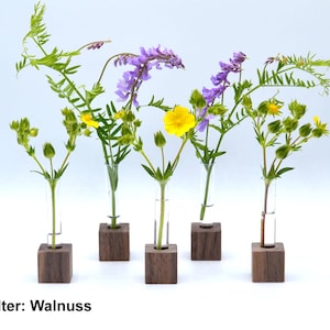 May include: Six small wooden cube holders with glass test tubes filled with wildflowers. The flowers are purple, yellow, and green. The text "Wuerfel-Halter: Walnuss" is printed below the holders.