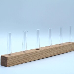 May include: A wooden stand with six clear glass test tubes. The stand is made of light brown wood and has a rectangular shape.