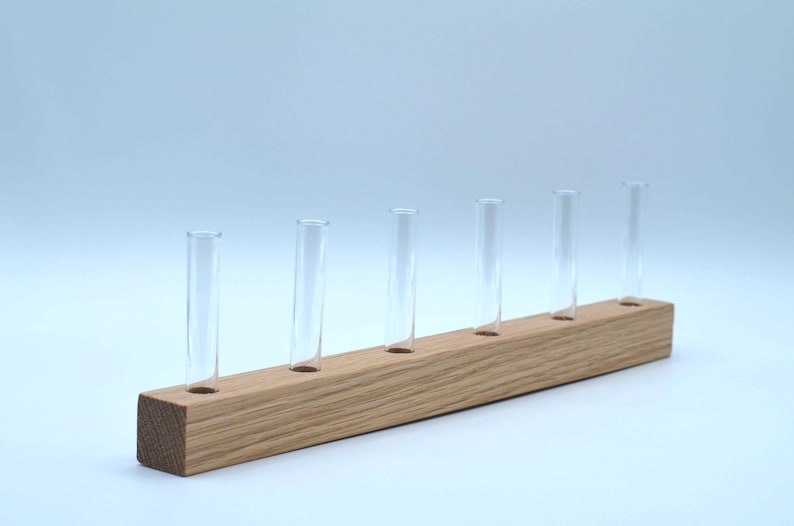 May include: A wooden stand with six clear glass test tubes. The stand is made of light brown wood and has a rectangular shape.