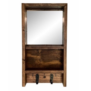 May include: A dark-stained wooden wall shelf with a rectangular mirror. It features a lower compartment and two black metal hooks. The wood grain is visible, giving it a natural, handcrafted appearance. A practical storage solution.