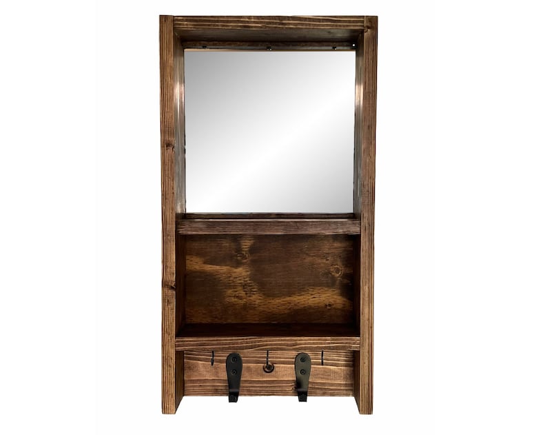 May include: A dark-stained wooden wall shelf with a rectangular mirror. It features a lower compartment and two black metal hooks. The wood grain is visible, giving it a natural, handcrafted appearance. A practical storage solution.