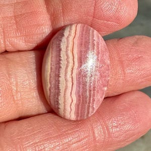 May include: A pink and white striped oval cabochon gemstone with a shiny, polished surface.